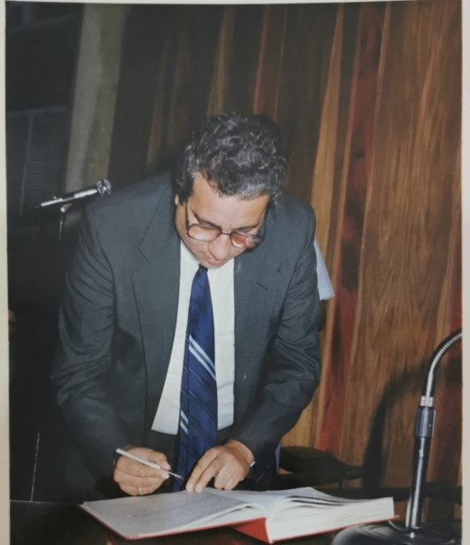 Antonio Rojas García firma un documento en un acto oficial.